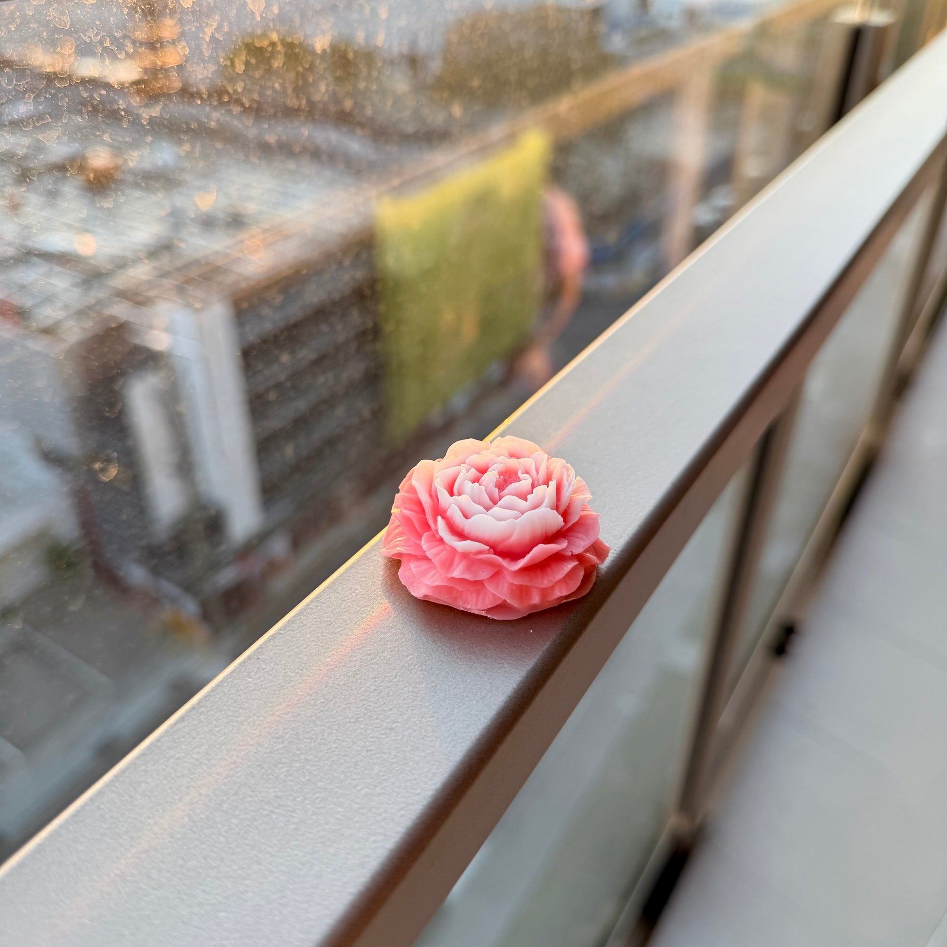 Pink flower candle on a window sill with a blurred outdoor background

