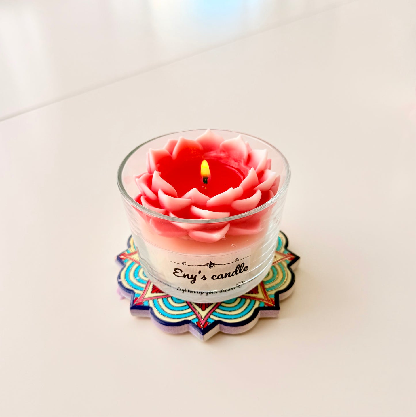 Pink flower-shaped candle in a glass jar on a colorful coaster with a white background

