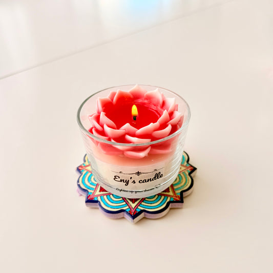 Pink flower-shaped candle in a glass jar on a colorful coaster with a white background

