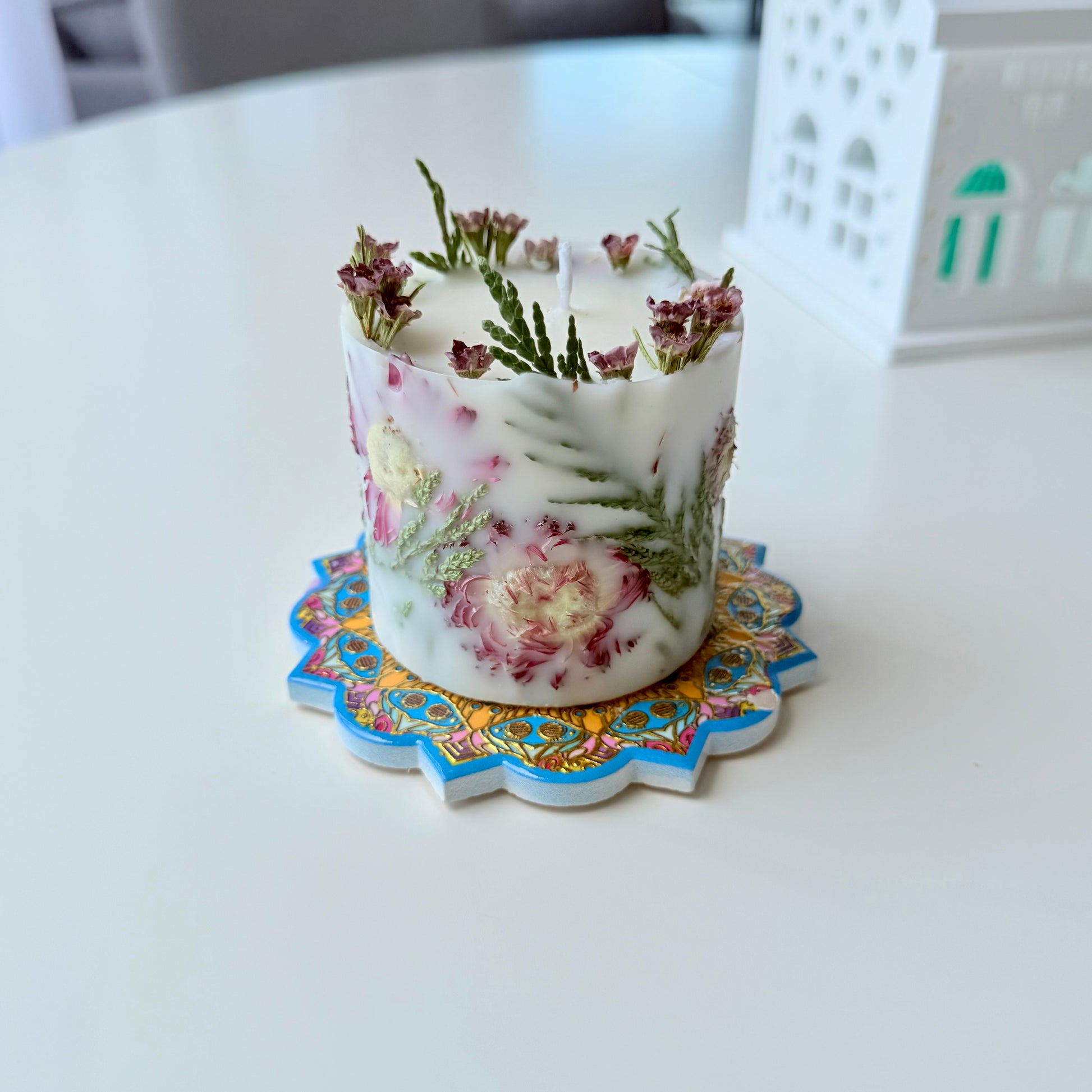 Decorative candle with floral design on a colorful coaster on a white surface
