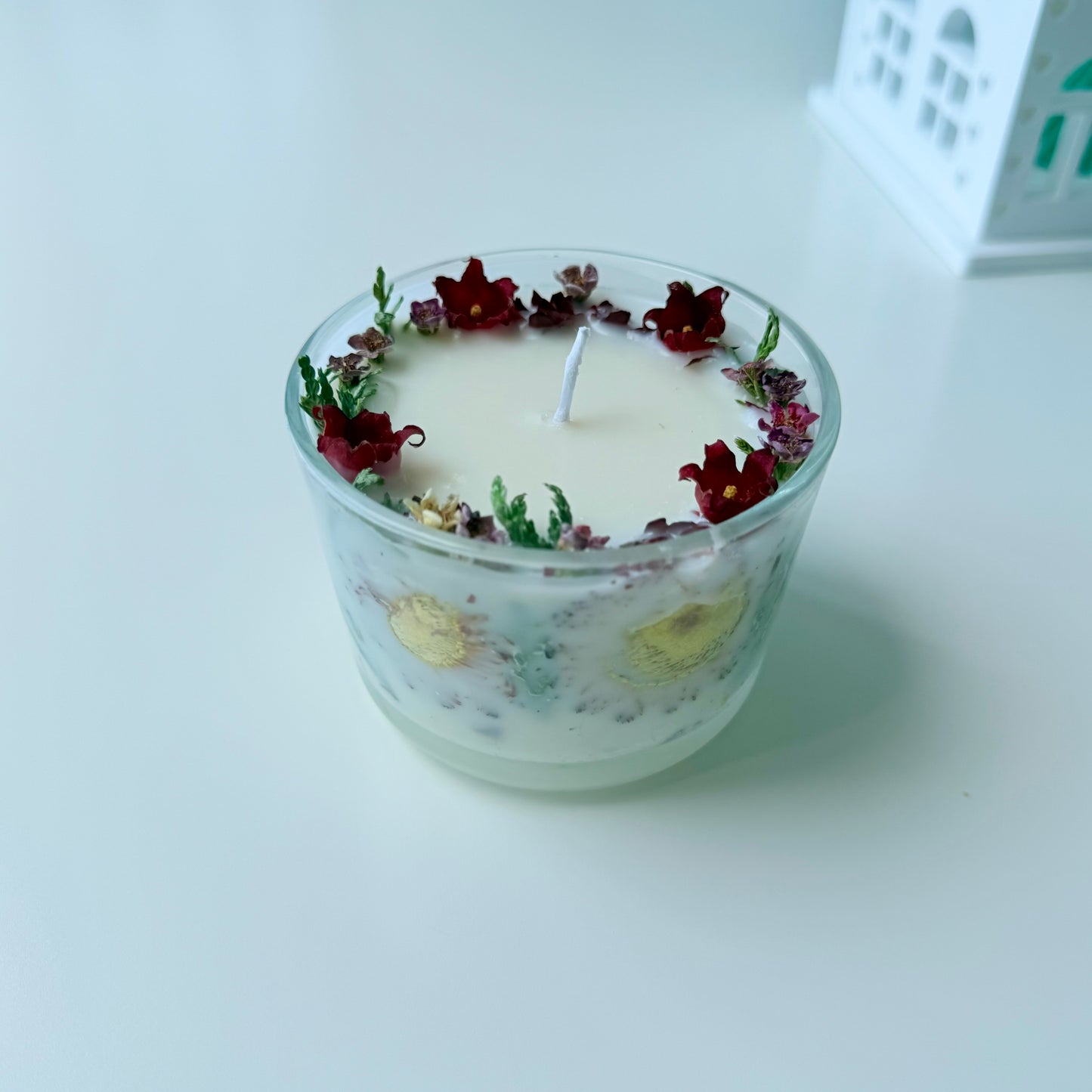 Candle in a glass container with floral decorations on a white surface